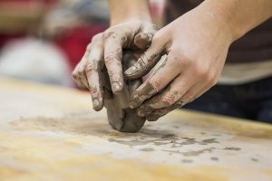 Person formt Ton mit ihren Händen auf einem Holztisch