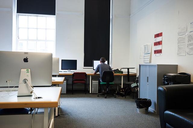 office with empty desks and computers with one lone worker