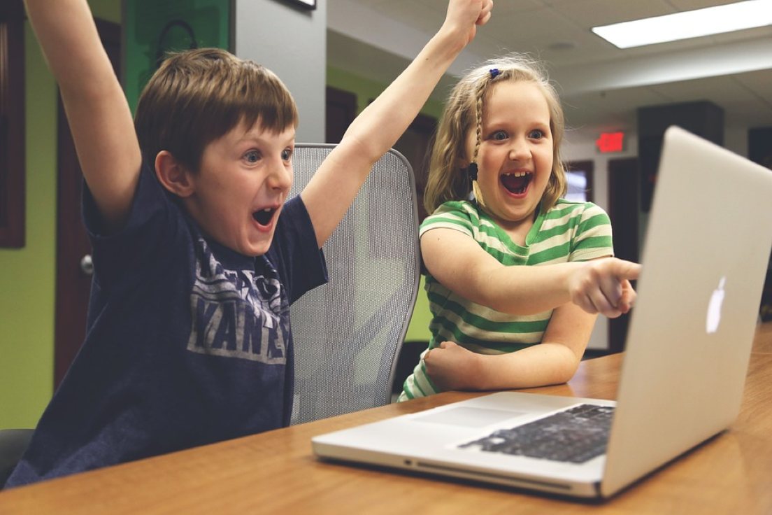 two kids excitedly look at the same laptop screen