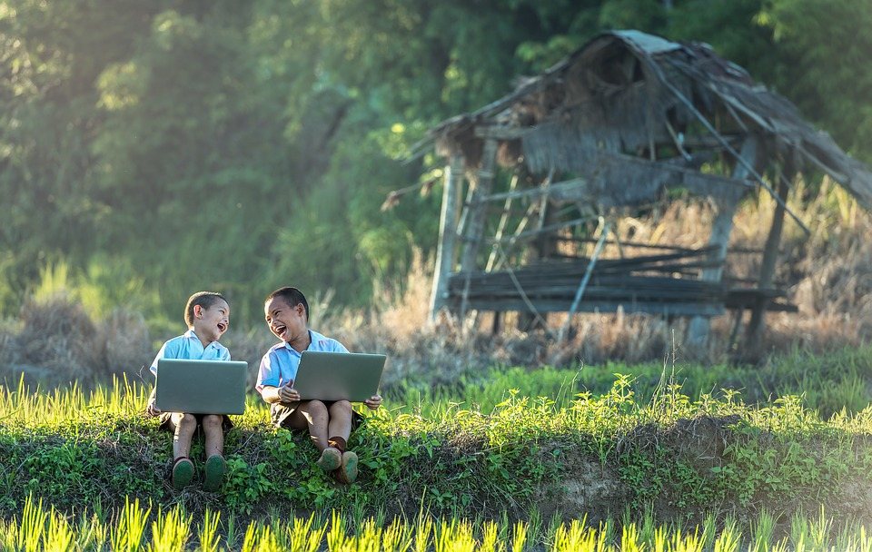 two children sitting outdoors with laptops on a conference call