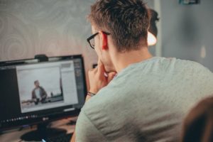 Over the shoulder view of man working at his desktop, looking at screen while in a thoughtful, pensive position