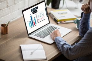 Side view of man working on a presentation on laptop at desk in well-lit office