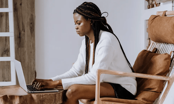 Full side view of relaxed young woman on chair sitting at table and typing on laptop in cozy, communal office space