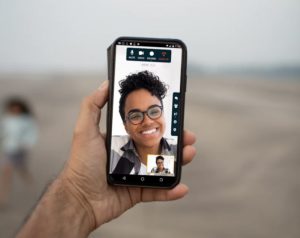 Close up view of a man’s hand holding a forward-facing device with 3 happy family members engaged in a video conference