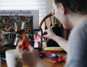 Side view of man setting up handheld device during a video call making origami cranes and chatting with friend