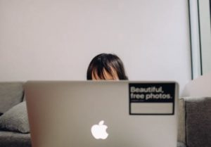 Straight on view of open laptop with only woman’s forehead visible on the other side as she works from home on couch