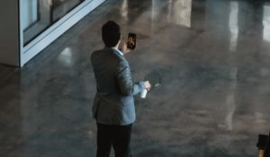 Wide shot of the backside of a man engaged in a video chat on mobile in lobby of building