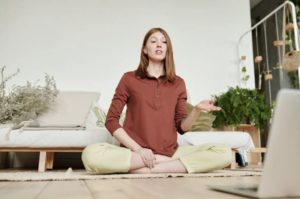Yoga instructor in lotus position on ground interacting with laptop in front of her and leading a class