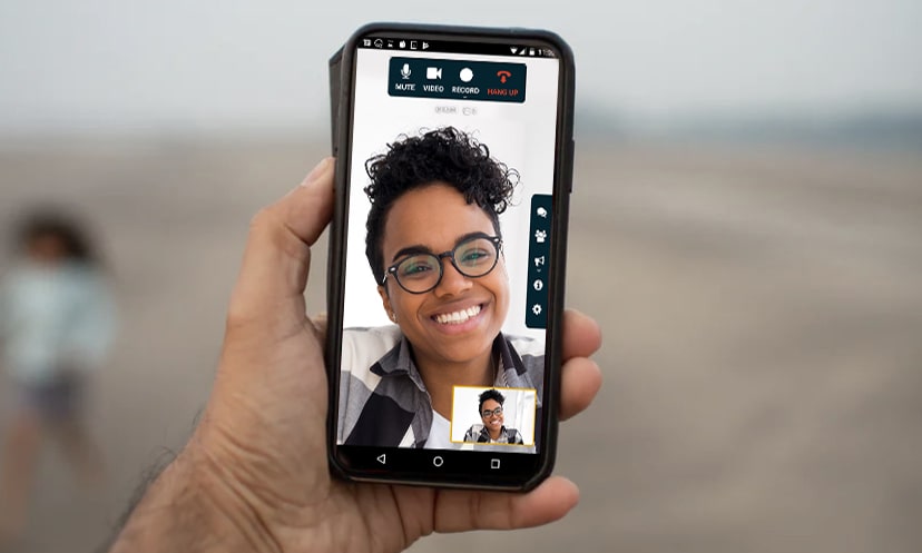 tile Close up view of a man’s hand holding a forward-facing device with 3 happy family members engaged in a video conference