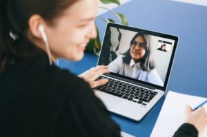 Pogled čez ramo na mlado žensko, ki uporablja prenosni računalnik, za videokonferenco med vrstniki med študijem in beleženjem