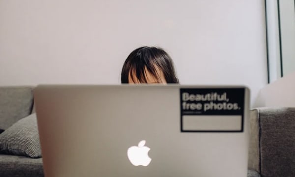 Straight on view of open laptop with only woman’s forehead visible on the other side as she works from home on couch copy-min