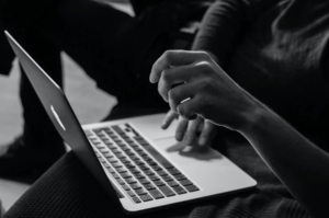 Black and white side angle of hands using laptop opened on person’s lap-min