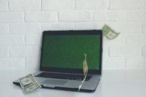 View of opened laptop against white brick wall with money floating around it