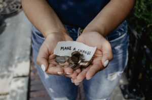View of woman’s hands holding out coins at waist level with a little note saying, “Make a change