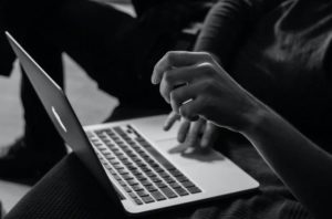 Black and white view of person sitting with laptop on lap, using one hand to navigate and the other in the foreground resting
