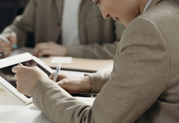 Side view of focused business woman seated at table beside a colleague in front of tablet holding a pen