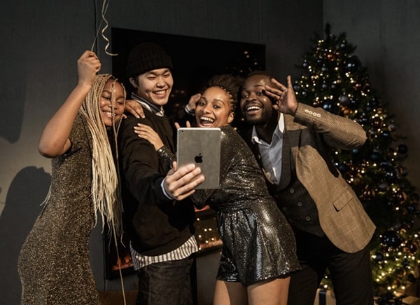 Four happy people, standing, laughing and having a party while video chatting with others using a tablet