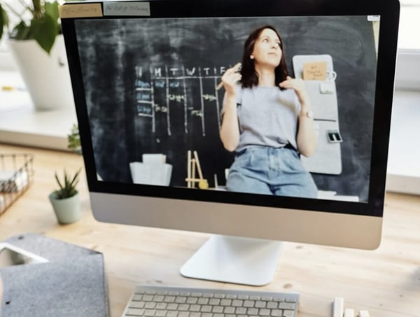 Close up view of desktop monitor displaying teacher lecturing in front of blackboard via video chat