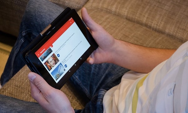 View of man holding tablet on lap while reclined on couch, looking through YouTube videos