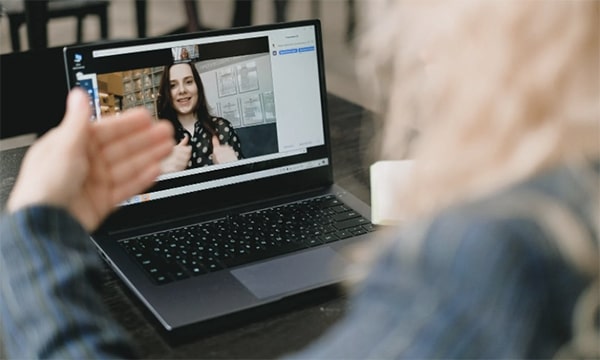 Over the left shoulder image of person using hand movements to communicate with a woman onscreen on laptop via video chatting